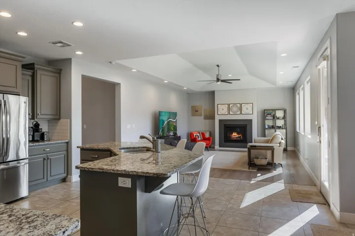 Open-concept living area featuring a kitchen with gray cabinetry and granite countertops, stainless steel appliances, a fireplace, and wood-finish flooring in the living space