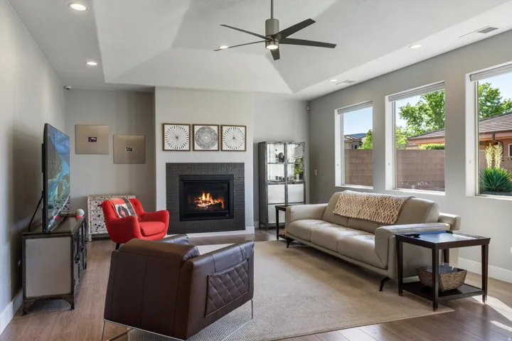 Recessed lighting illuminates a living space featuring a vaulted ceiling with a ceiling fan, a fireplace with a dark surround, and multiple windows