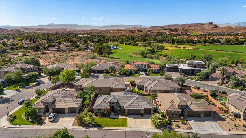 Residential street with multiple properties featuring mature landscaping, paved driveways, and attached garages