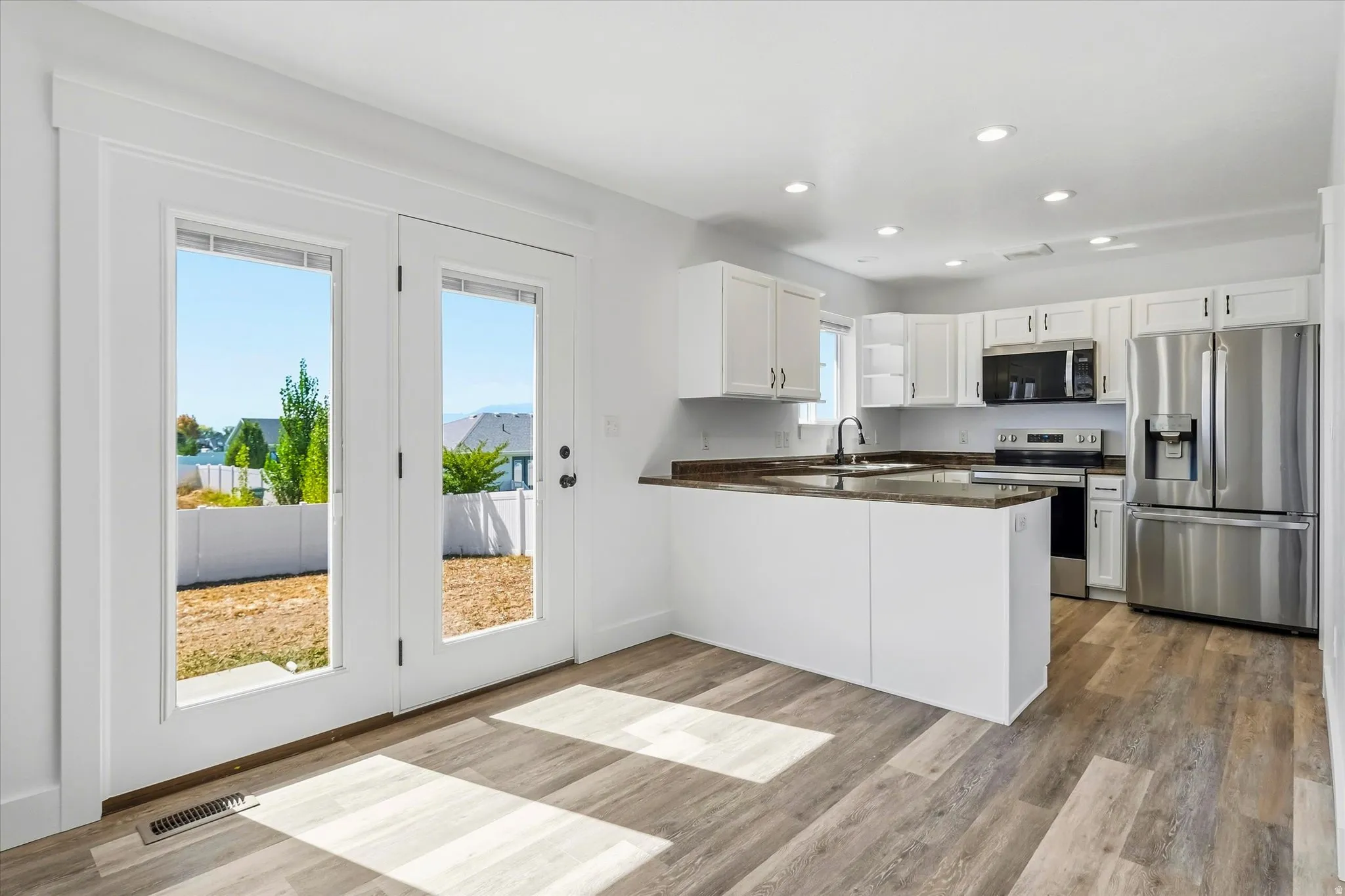 Open-concept kitchen with white cabinetry, stainless steel appliances, and hard flooring