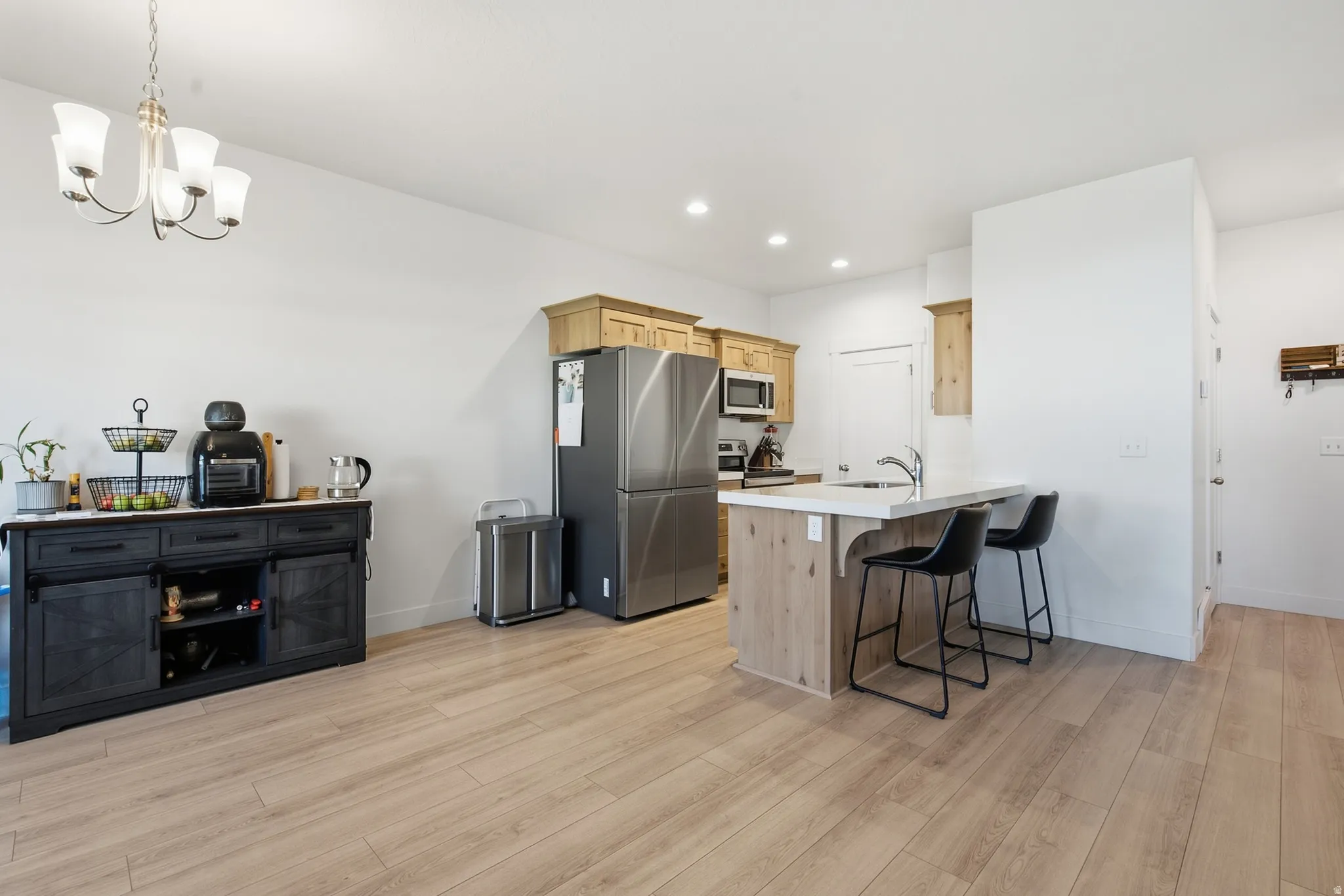 Kitchen featuring wood-finish flooring, recessed lighting, a kitchen island with seating, a stainless steel refrigerator, and wood cabinetry