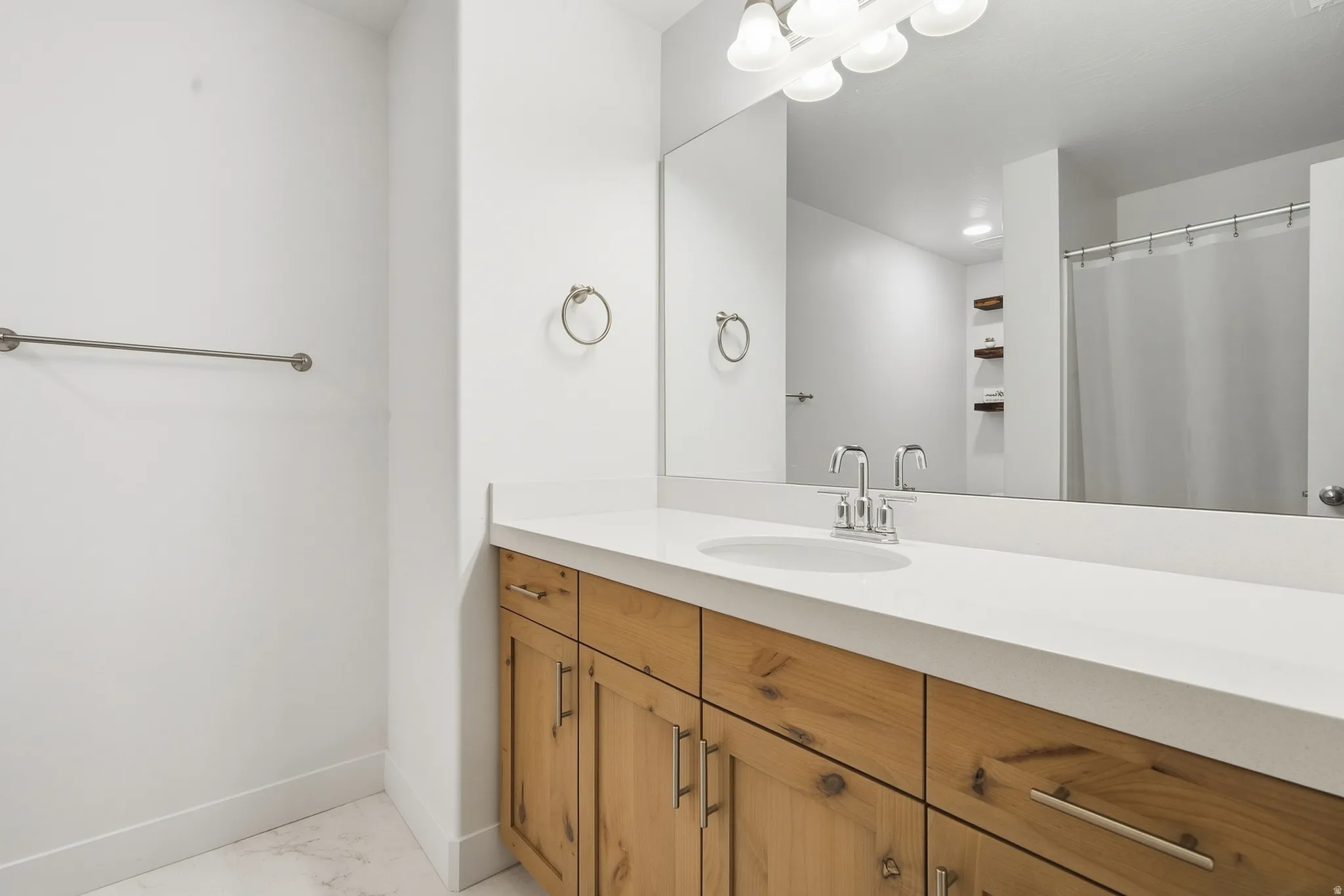 Wood-finish vanity with an integrated sink, polished chrome faucet, and expansive wall-mounted mirror
