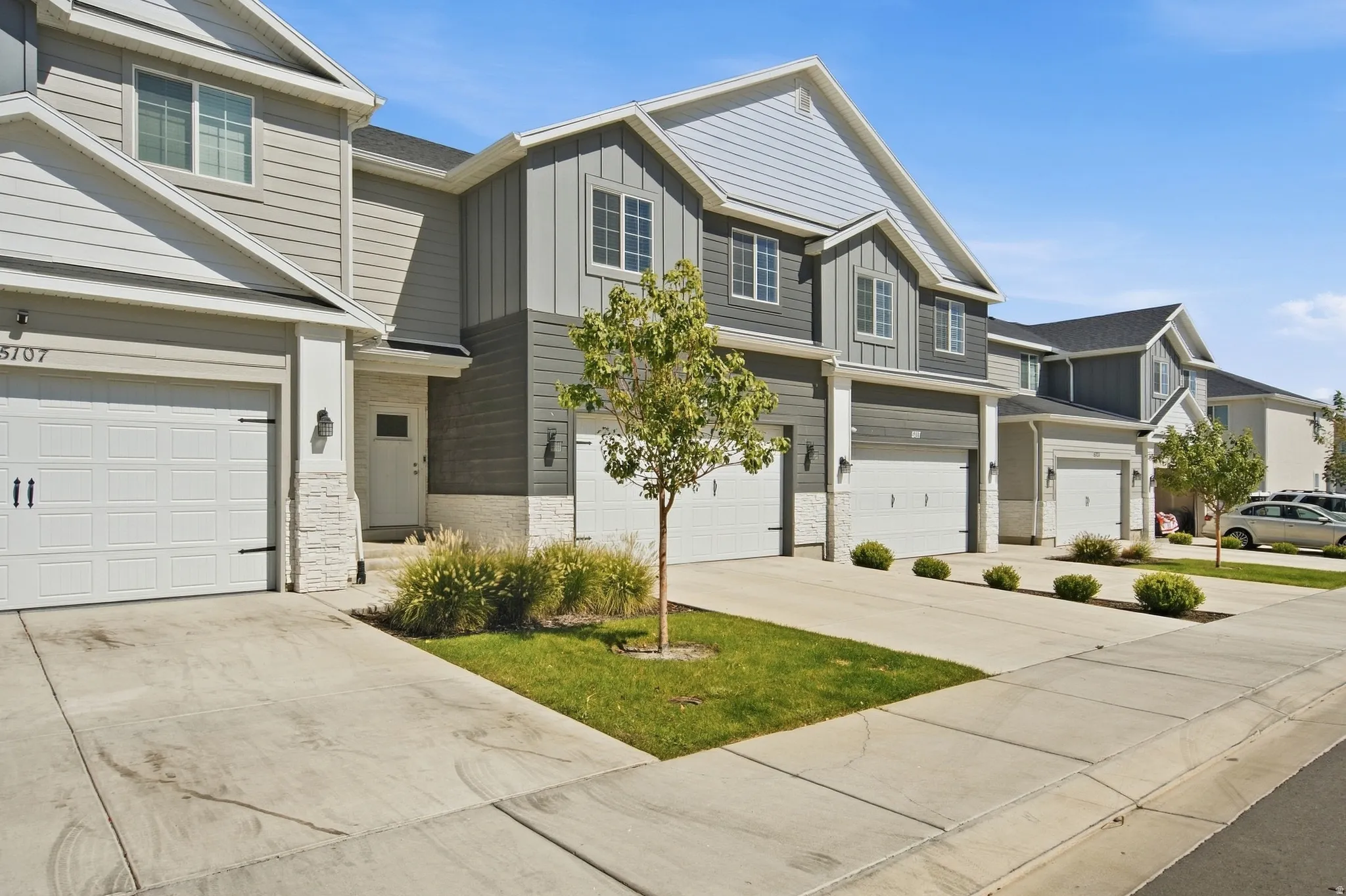 Modern townhome exterior featuring light and dark gray siding, white garage doors with black hardware, and stone veneer accents