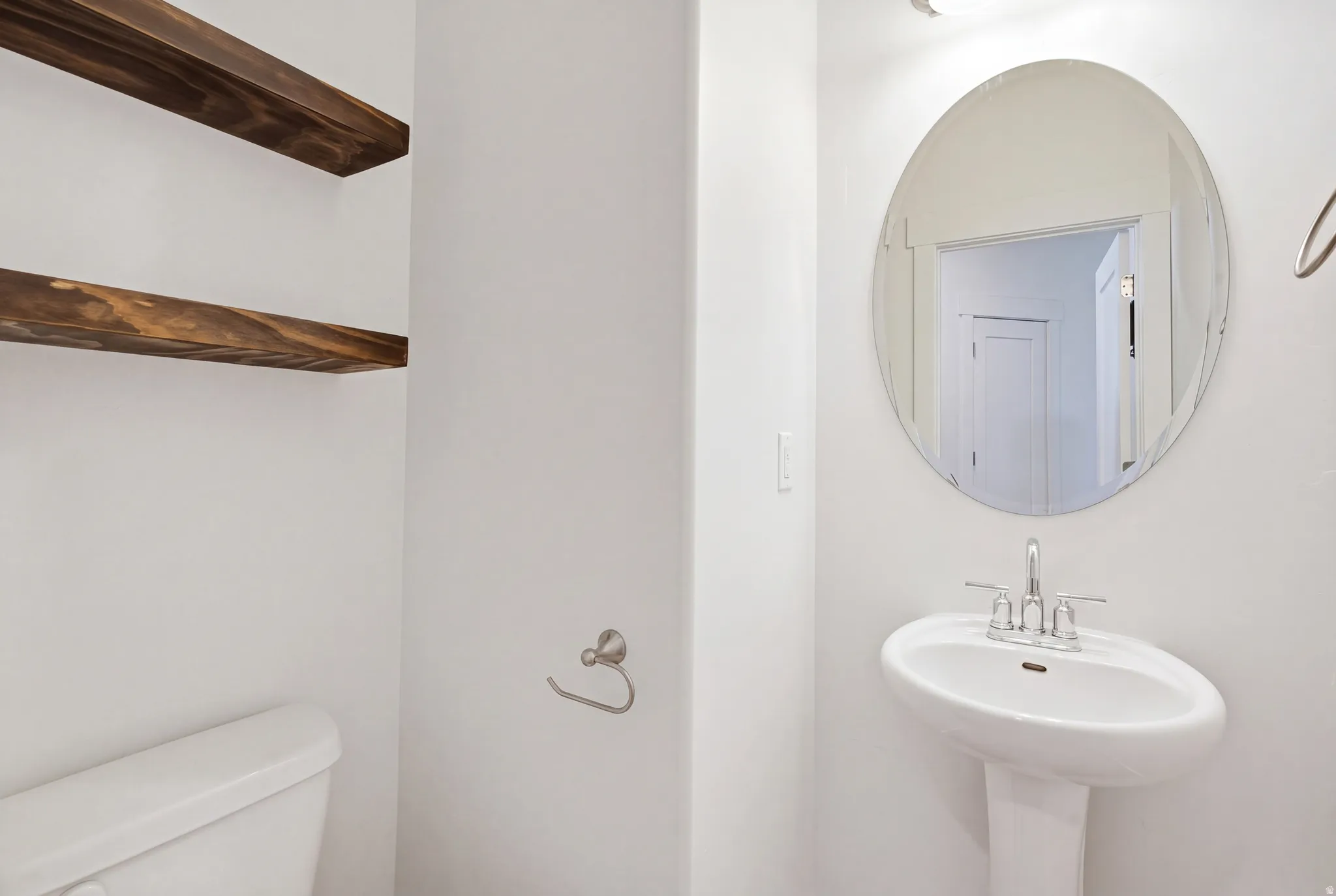 Pedestal sink with chrome faucet, oval mirror, and floating wood shelves