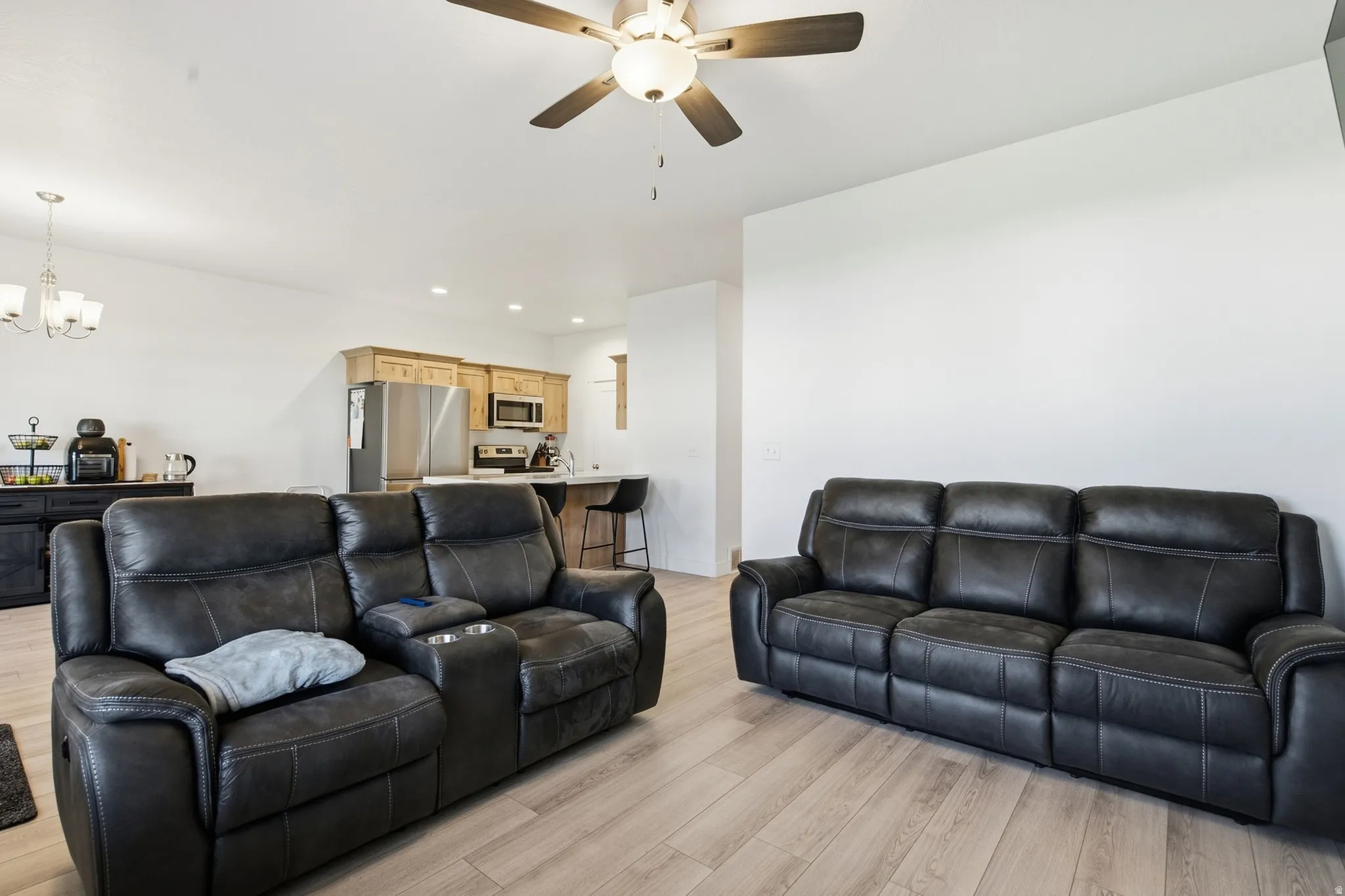 Open-concept living area with light wood-finish flooring, a ceiling fan, and recessed lighting