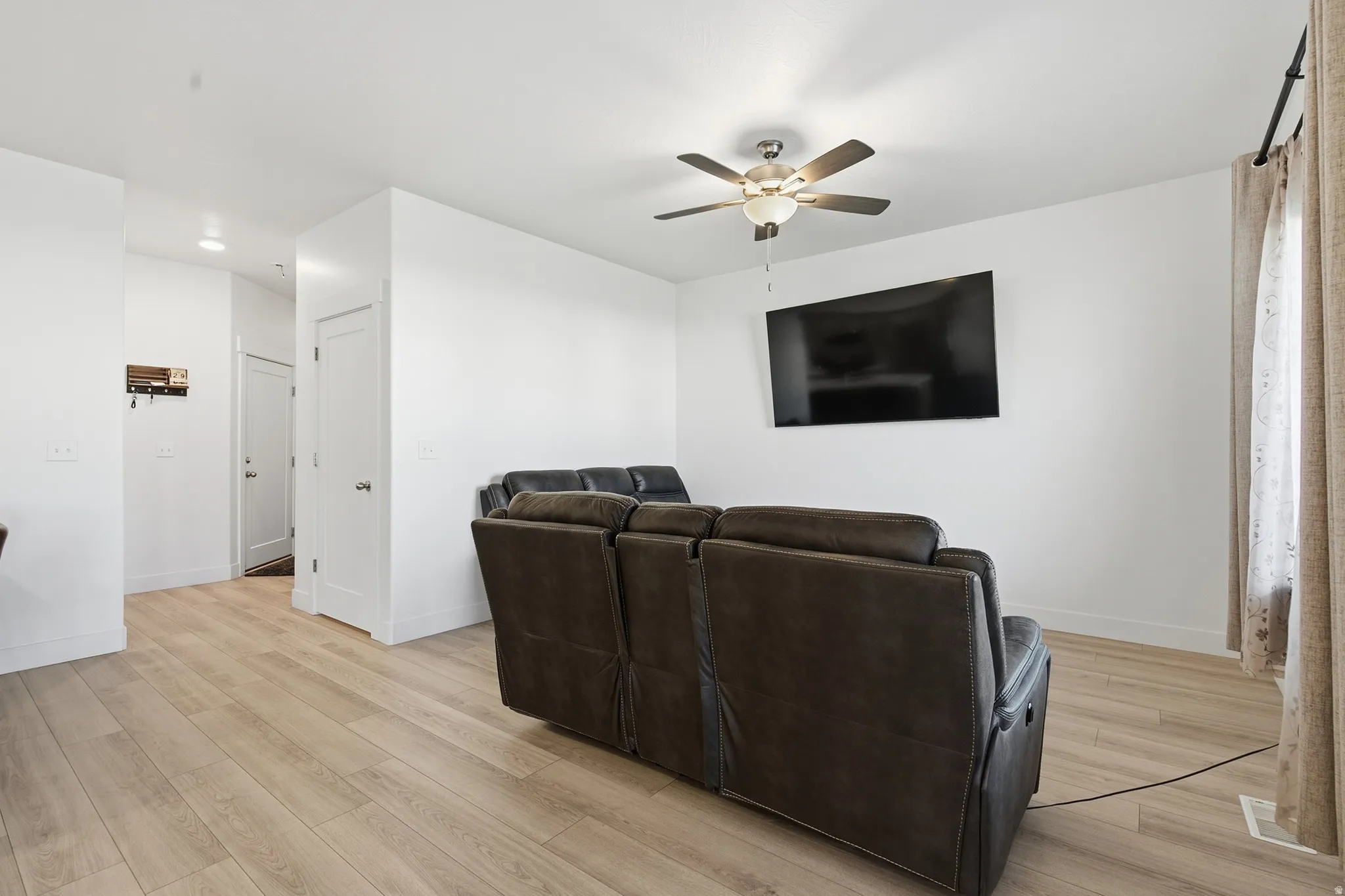 Wood-finish flooring throughout, bright white walls, and a ceiling fan with integrated lighting