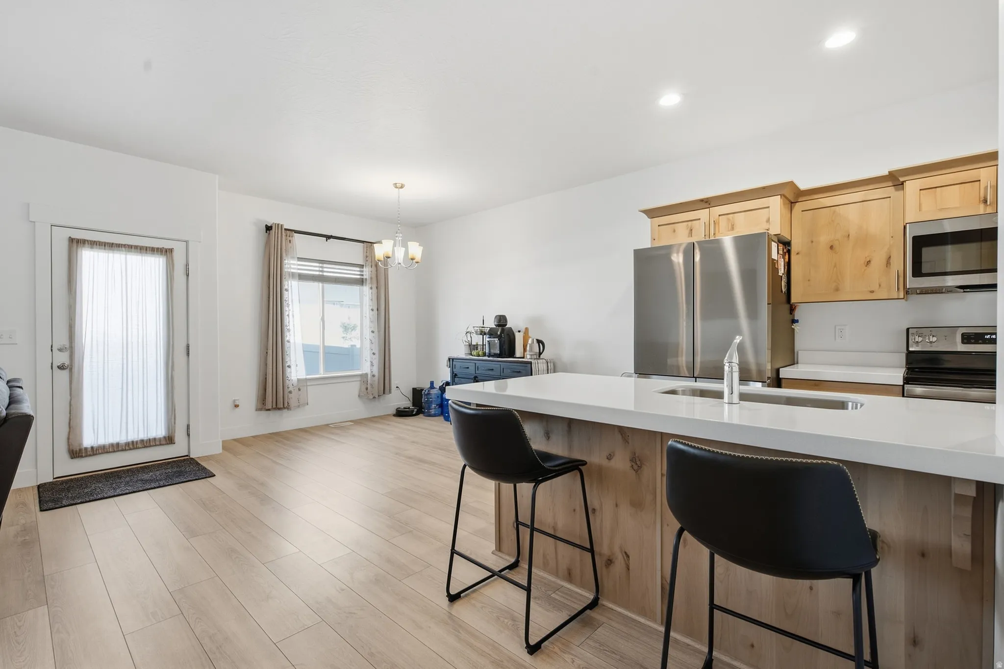 Wood-finish flooring throughout, kitchen featuring light wood cabinetry, stainless steel appliances, and a solid surface countertop with an integrated sink