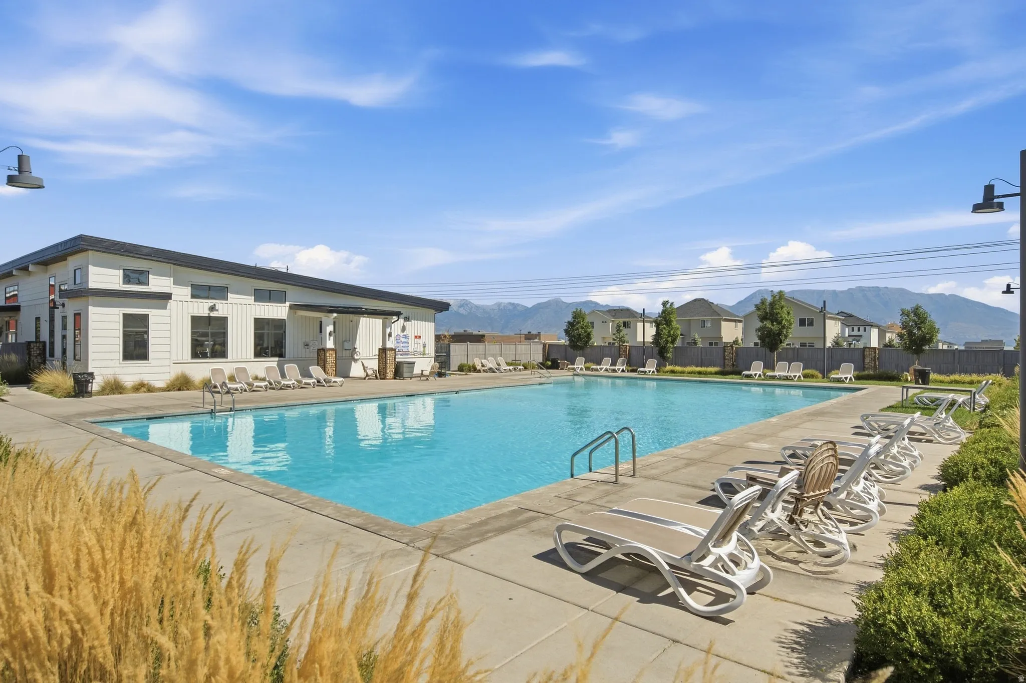 Expansive outdoor swimming pool with concrete decking, surrounding lounge seating, and a modern building featuring a covered entry