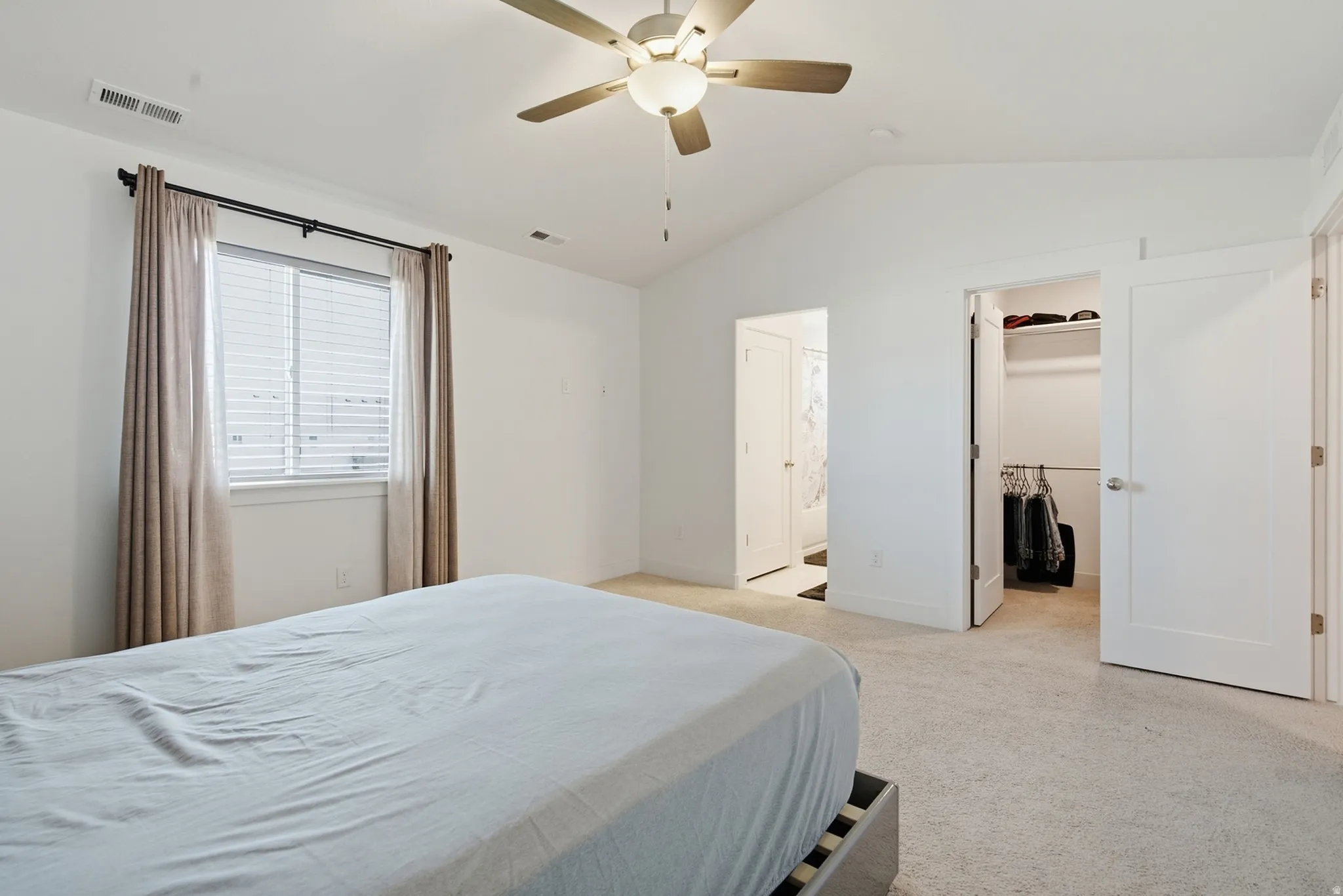 Carpeted room featuring a vaulted ceiling, ceiling fan with light fixture, window with blinds, and a walk-in closet with shelving