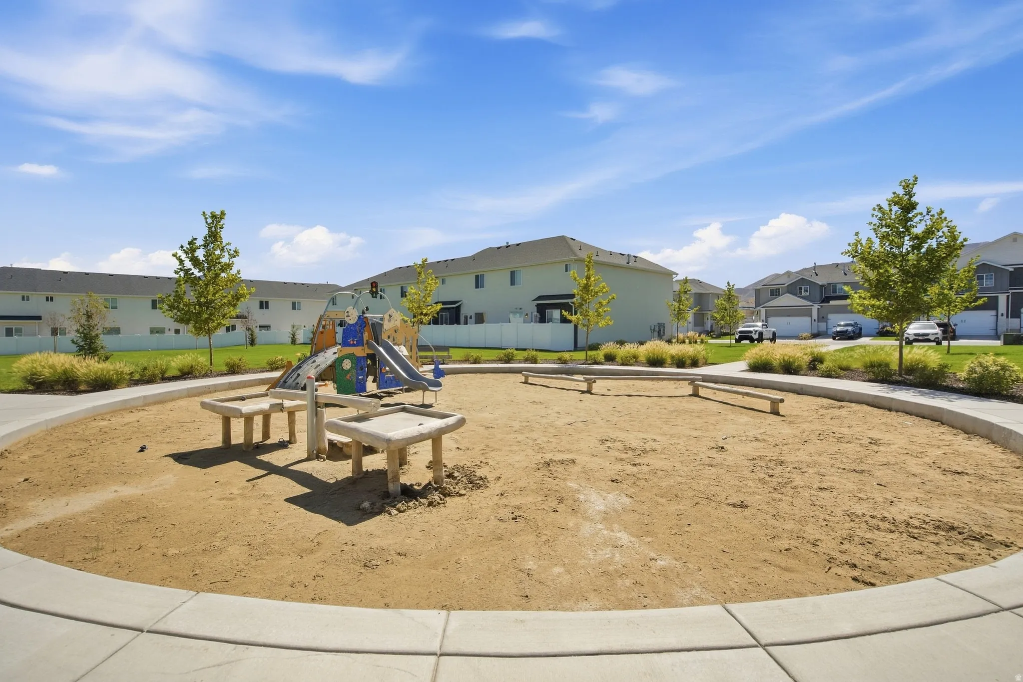 Community playground featuring a sand area, built-in play structure, and concrete benches