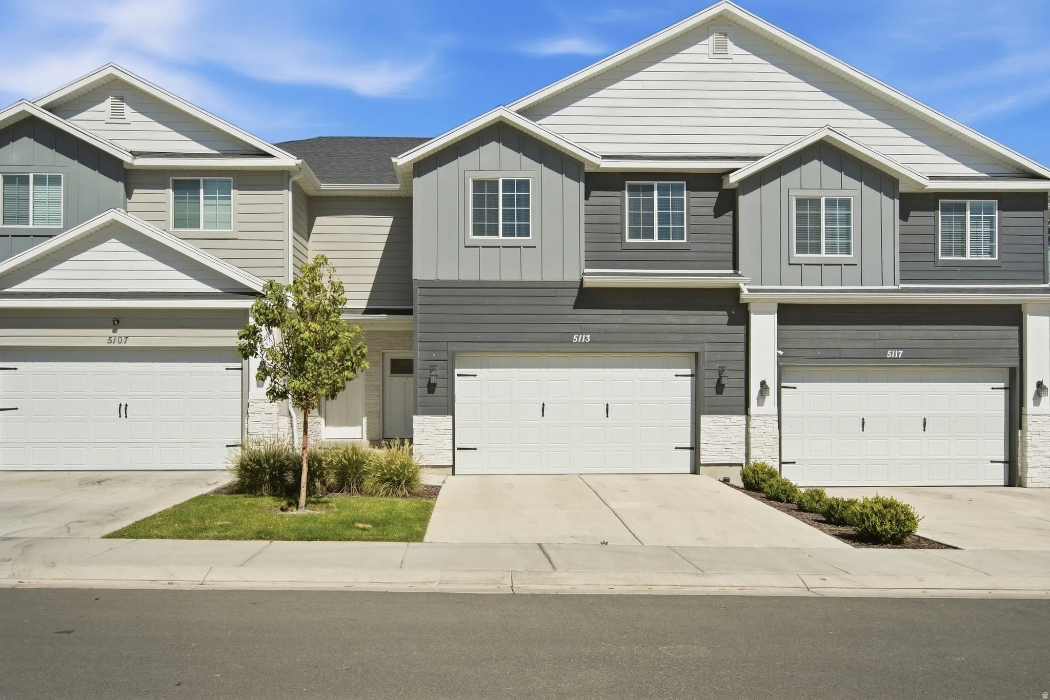 Contemporary exterior featuring multiple roof lines, a mix of horizontal siding and board-and-batten siding, white garage doors with black hardware, and integrated exterior lighting fixtures