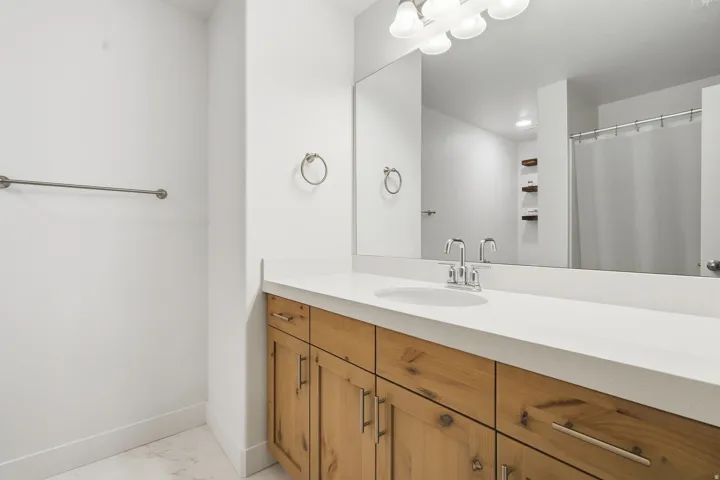 Wood-finish vanity with an integrated sink, polished chrome faucet, and expansive wall-mounted mirror