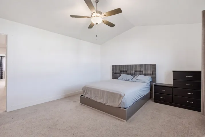 Vaulted ceiling, ceiling fan with integrated lighting, carpeted flooring, and white painted walls