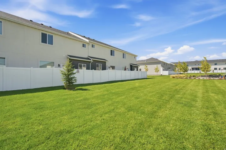 Expansive green space featuring a white vinyl fence, mature trees, and a landscaped garden bed
