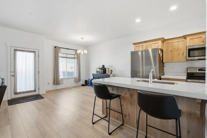 Wood-finish flooring throughout, kitchen featuring light wood cabinetry, stainless steel appliances, and a solid surface countertop with an integrated sink