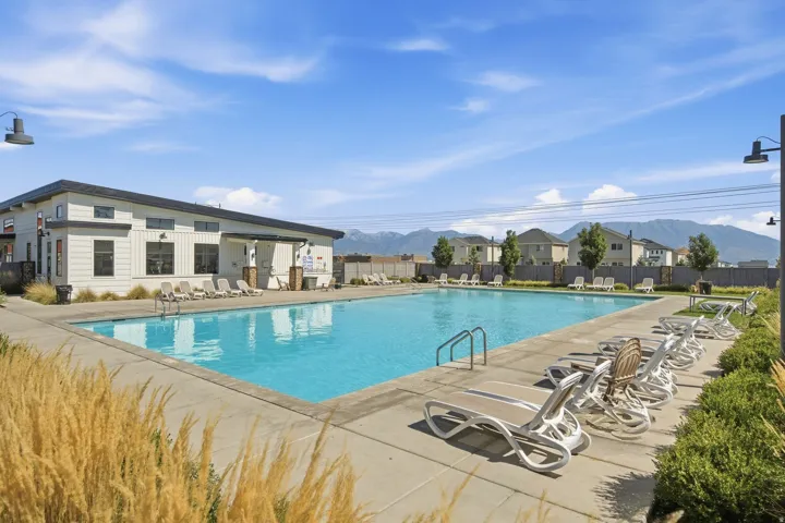 Expansive outdoor swimming pool with concrete decking, surrounding lounge seating, and a modern building featuring a covered entry