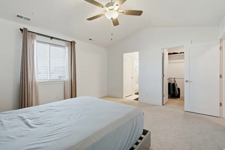 Carpeted room featuring a vaulted ceiling, ceiling fan with light fixture, window with blinds, and a walk-in closet with shelving