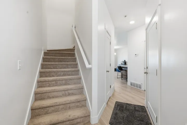 Carpeted staircase with a white handrail, light-toned wood-finish flooring, and white interior doors