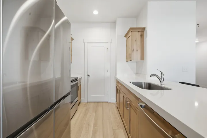 Stainless steel appliances, wood-finish flooring, undermount sink with chrome faucet, light wood cabinetry, and white countertops