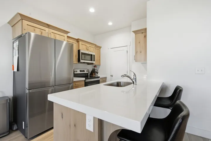 Kitchen featuring light wood cabinetry, white countertops, stainless steel appliances, and an integrated kitchen island with a sink