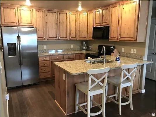 Kitchen featuring wood-finish flooring, granite countertops, wood cabinetry, a stainless steel refrigerator, and a kitchen island with a built-in sink