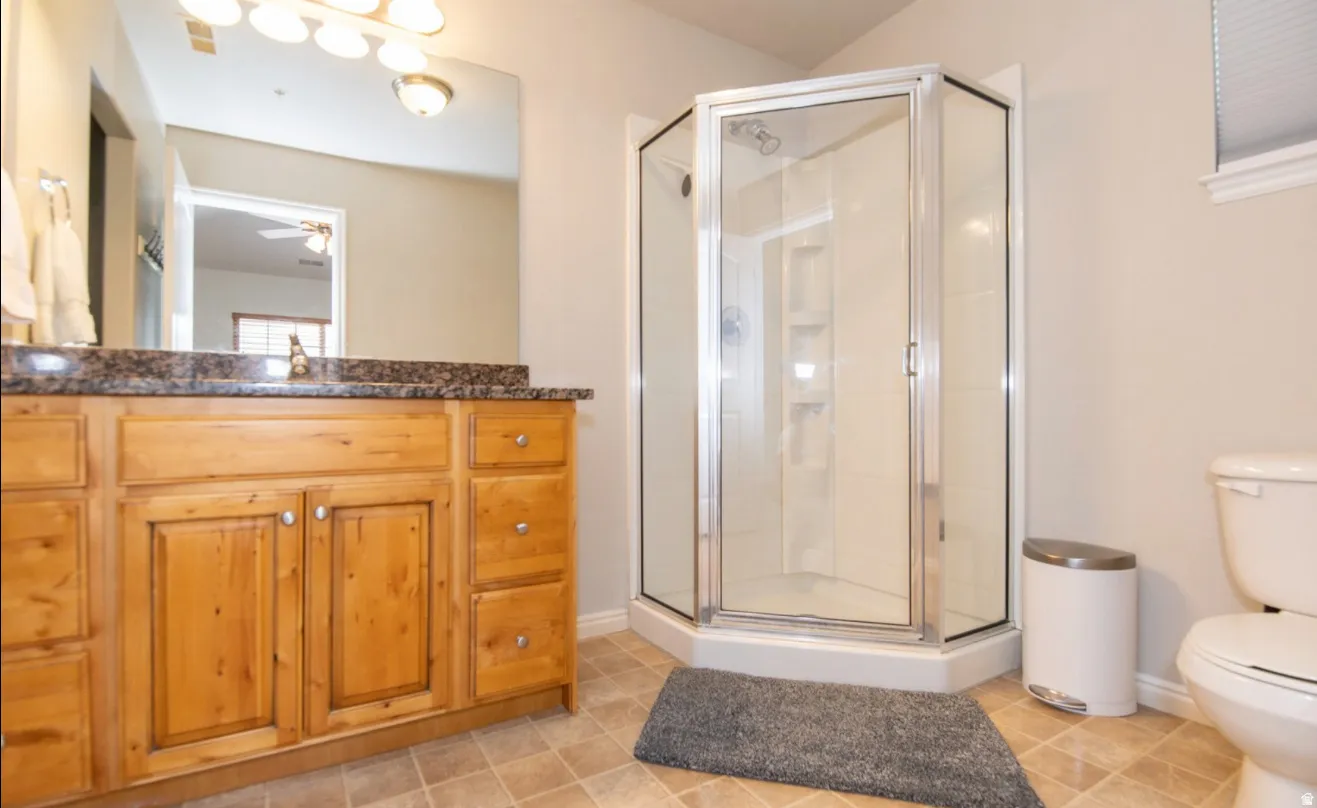 Wood vanity with multiple drawers, stone countertop, integrated sink, and an enclosed shower with a glass door
