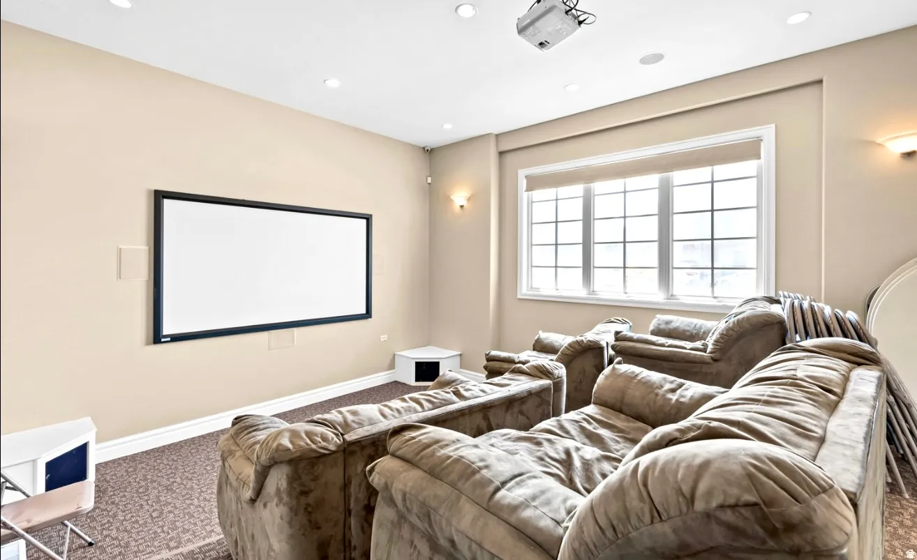 Dedicated media room featuring a mounted projection screen, recessed lighting, wall sconces, and a multi-pane window