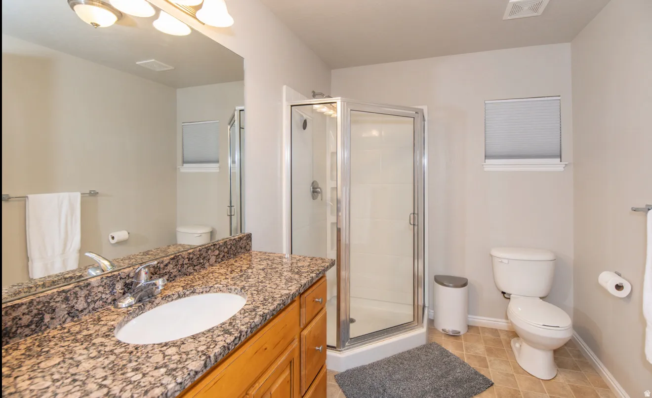 Shower enclosure with glass door, vanity with stone countertop, integrated sink, and light wood-finish cabinetry, and neutral wall paint