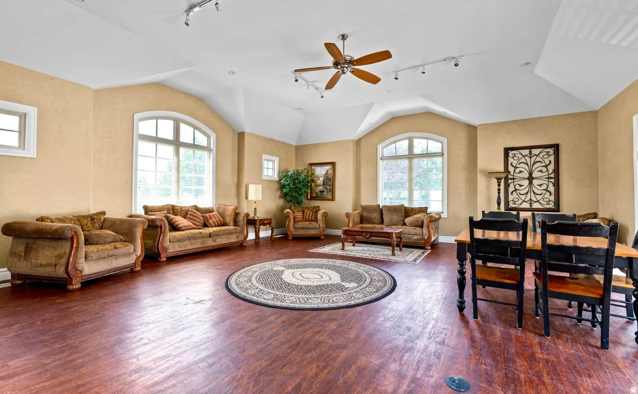 Wood-finish flooring, vaulted ceiling, arched window, ceiling fan, and track lighting
