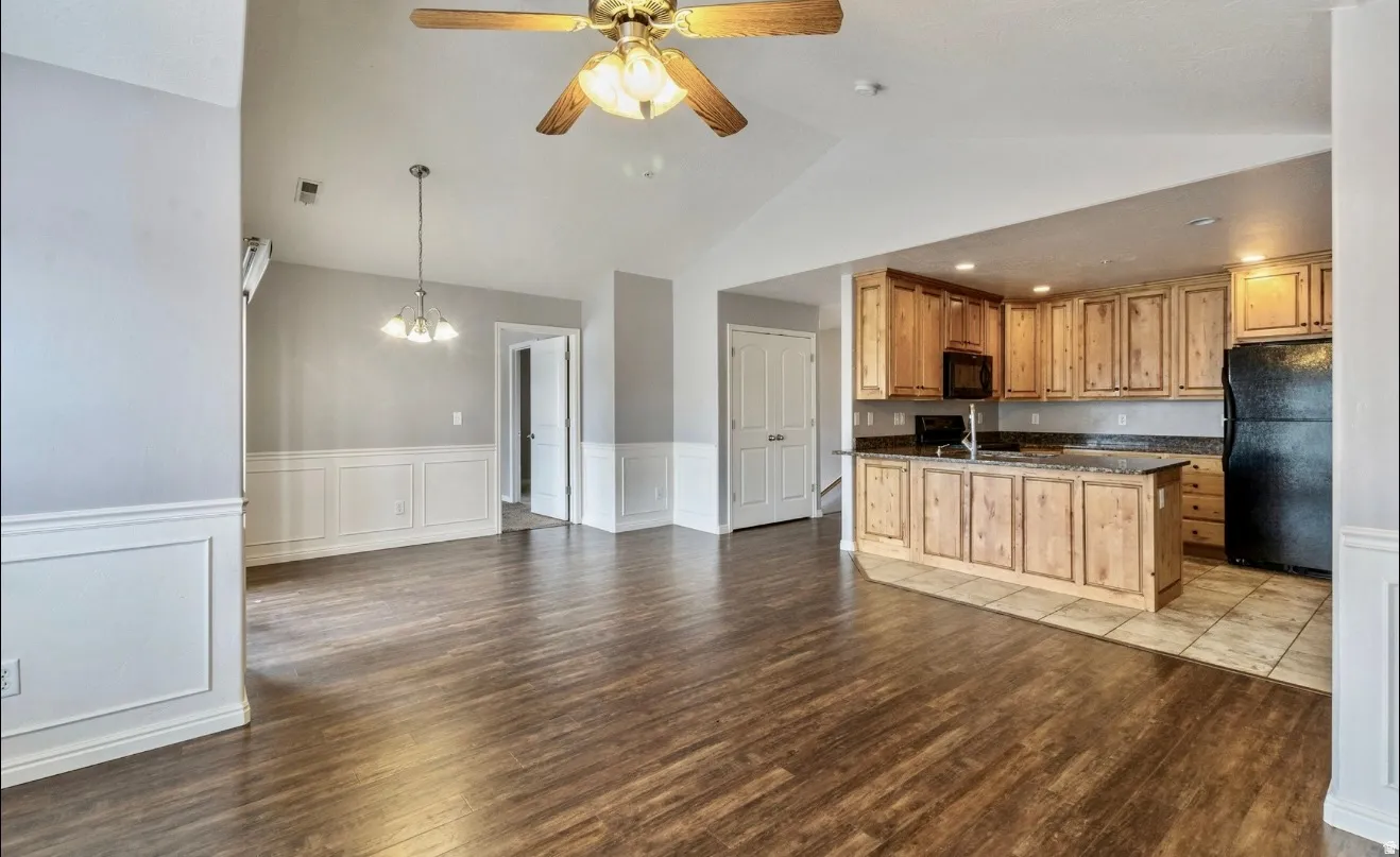 Vaulted ceiling with ceiling fan, wood-finish flooring, wainscoting, pendant lighting, and kitchen with wood cabinetry