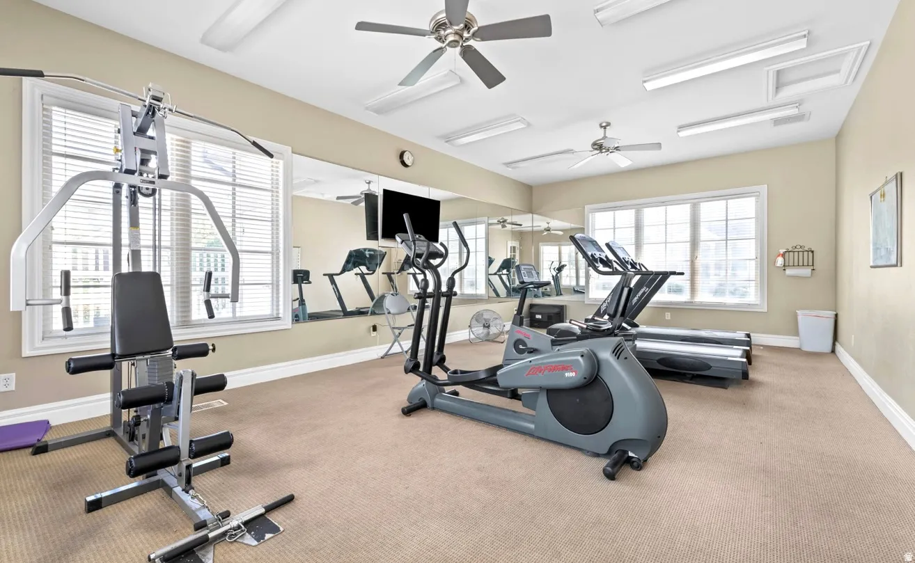 Carpeted fitness room featuring large windows, wall-mounted mirrors, ceiling fans, and recessed lighting