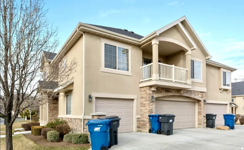 Stucco exterior with stone accents, multiple garage doors, and an upper-level balcony