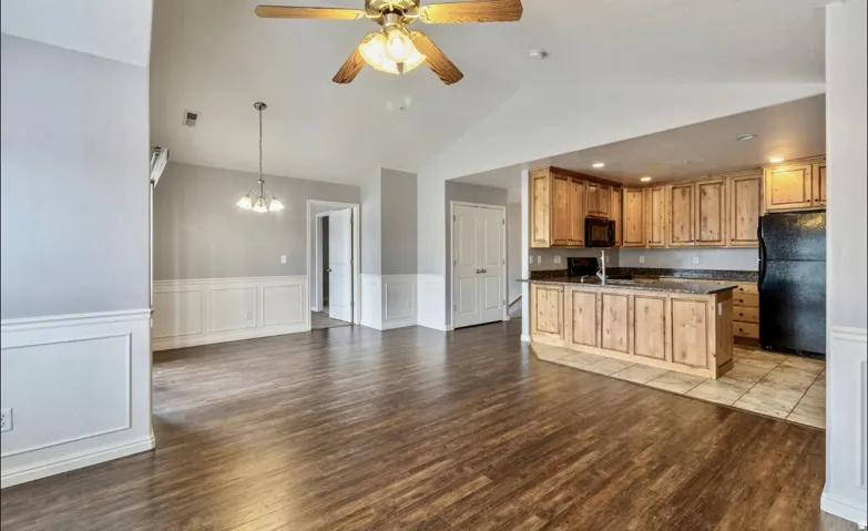 Vaulted ceiling with ceiling fan, wood-finish flooring, wainscoting, pendant lighting, and kitchen with wood cabinetry