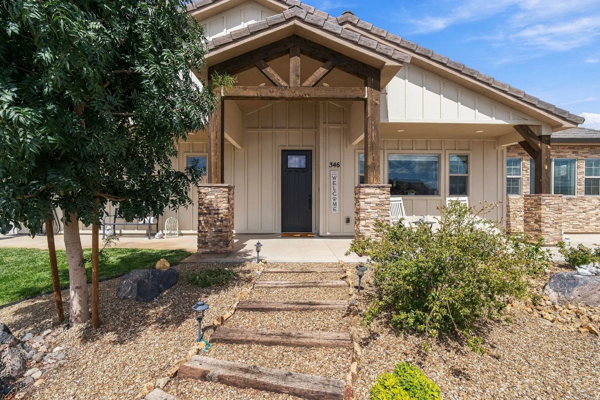 Board and batten siding with stone accents, covered front porch, exposed wood beam detailing, dark paneled entry door, and multi-pane windows