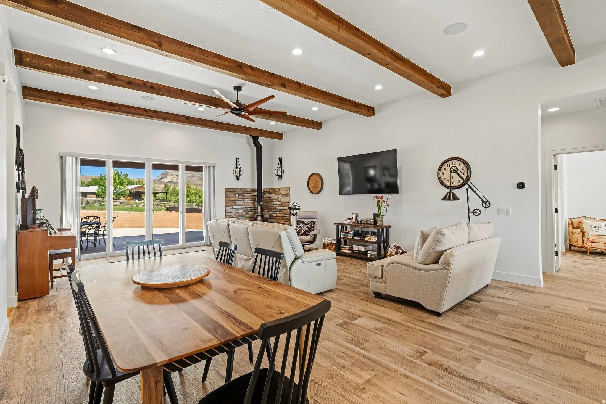 Vaulted ceiling with exposed wood beams, wood-finish flooring, sliding glass patio doors, and a stone-clad fireplace