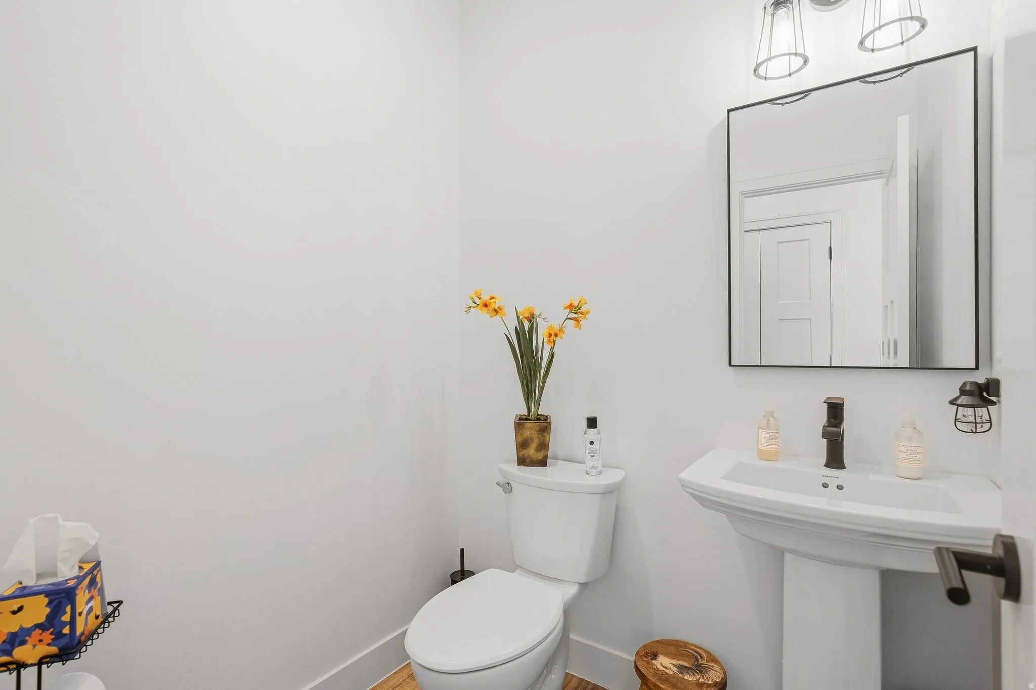 Pedestal sink, wall-mounted mirror, modern wall sconce, oil-rubbed bronze faucet, and wood-finish flooring