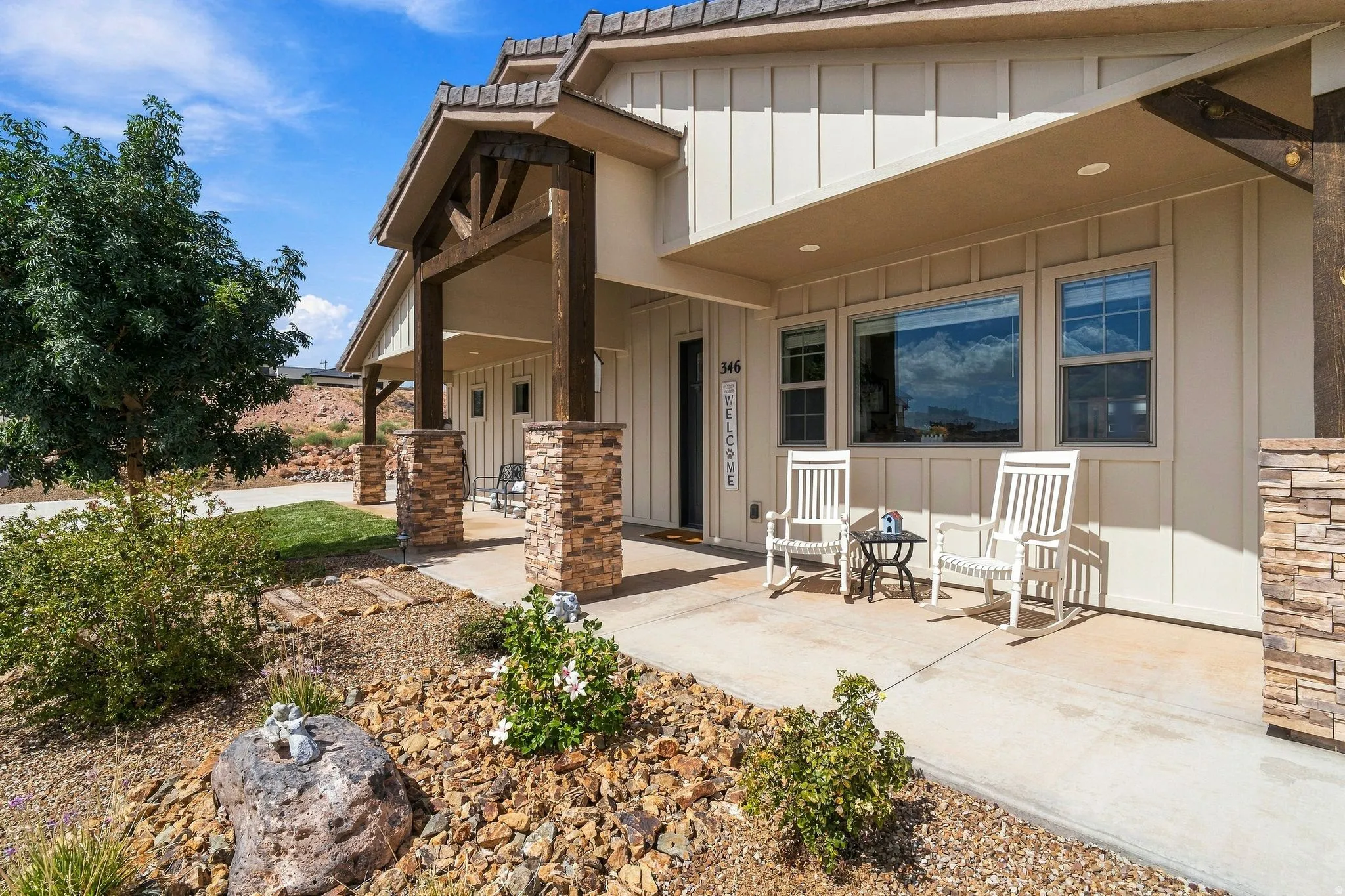 Board and batten siding, stone facade accents, covered front porch, concrete pathway, and xeriscaped front yard
