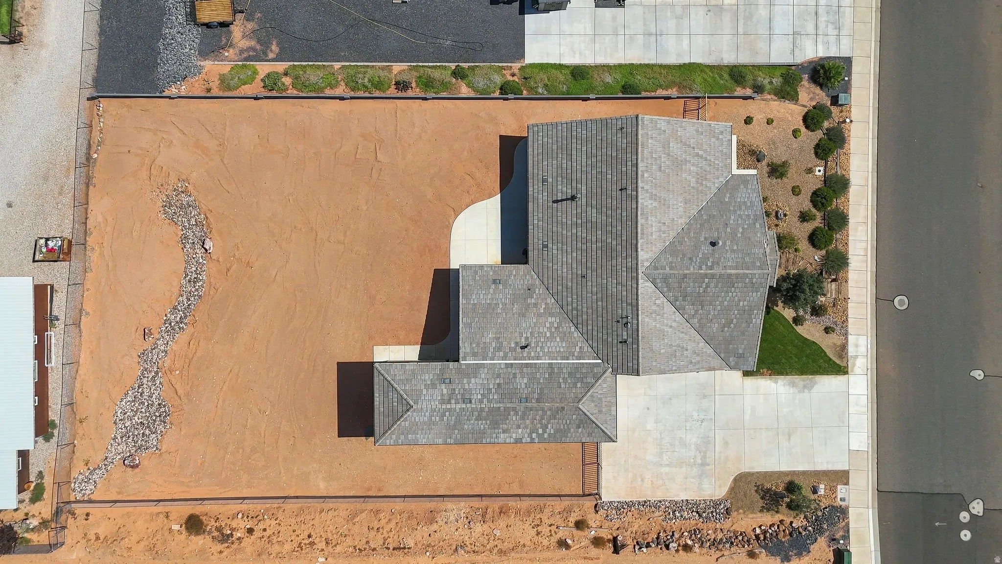 Large lot with a grey shingle roof, concrete driveway, and rock landscaping
