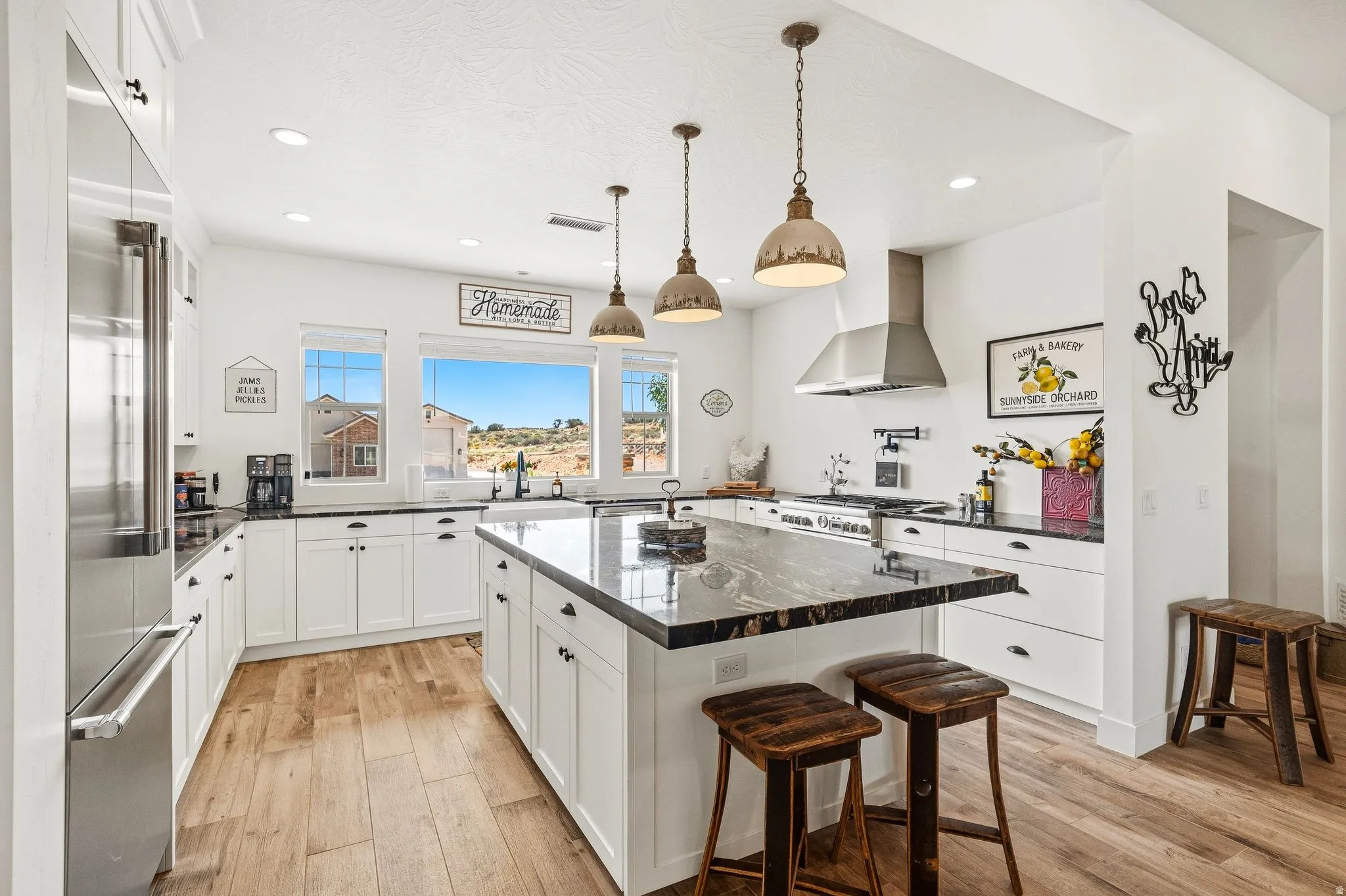 White cabinetry with black hardware, wood-finish flooring, a kitchen island with stone countertop, stainless steel appliances, and pendant lighting