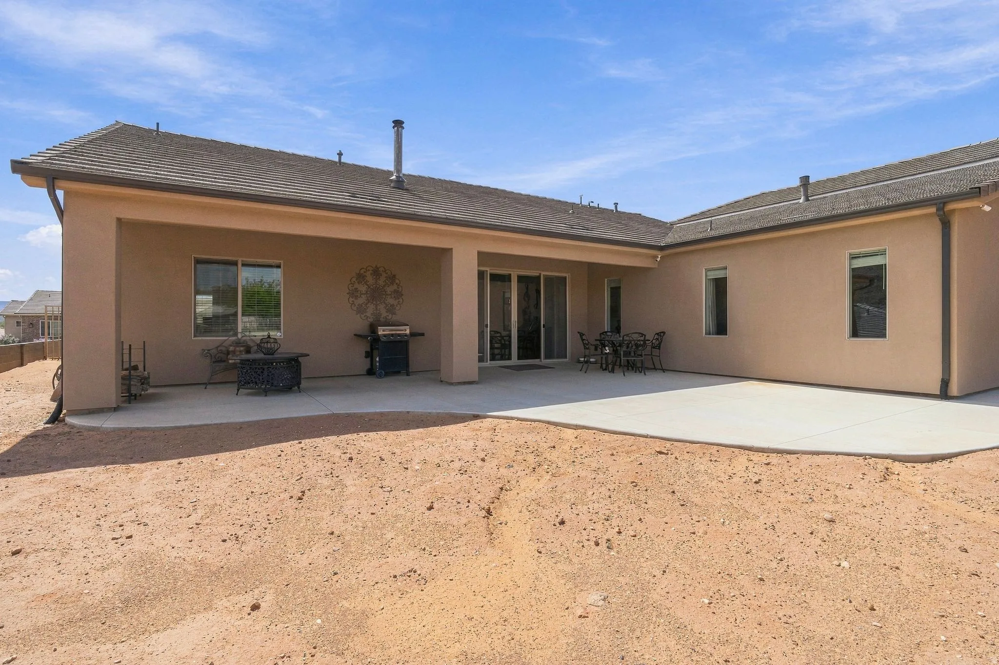 Expansive concrete patio with a covered outdoor area, sliding glass doors, and a neutral stucco exterior