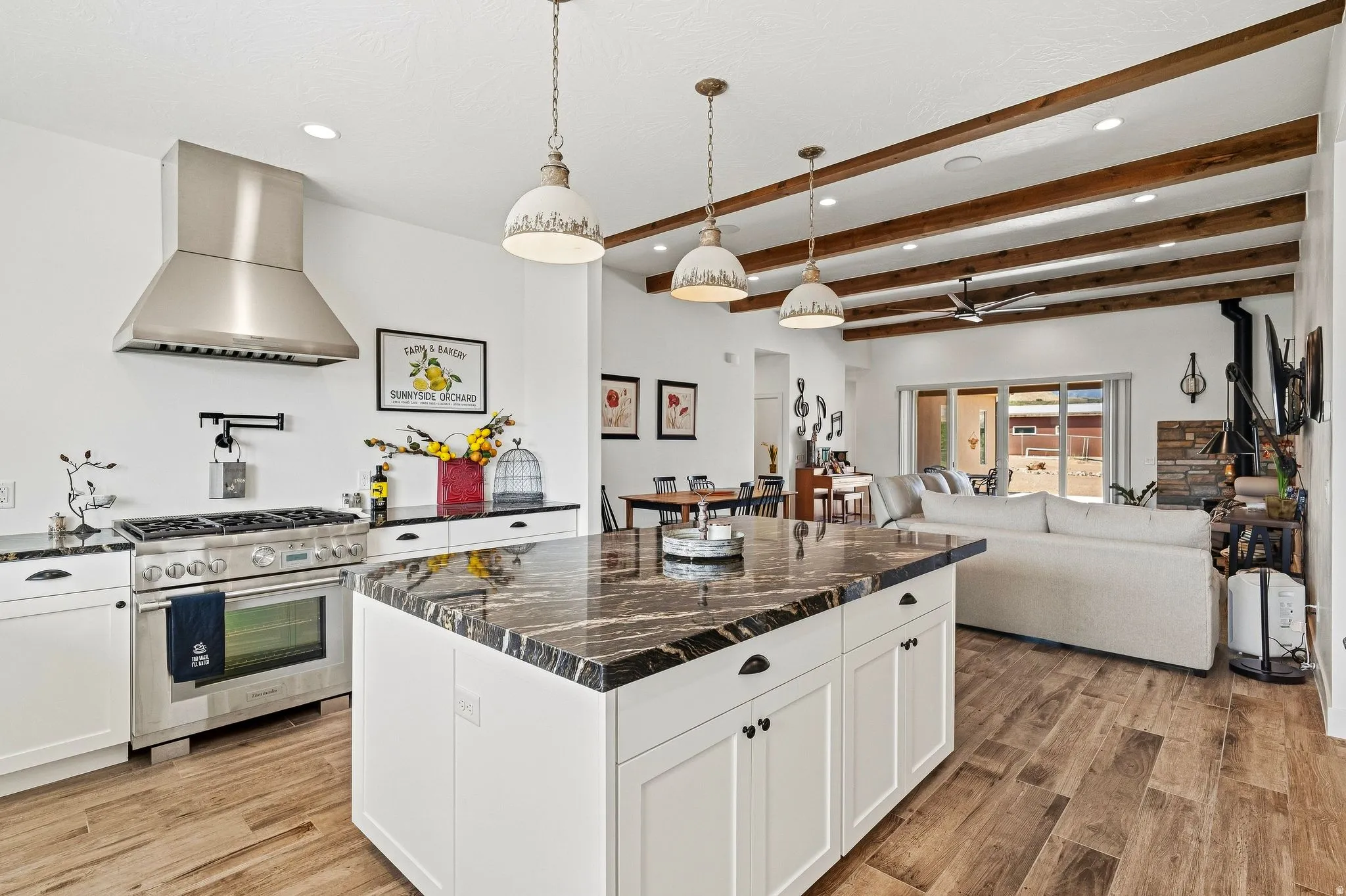 Gourmet kitchen featuring a stainless steel range with matching vent hood, a large island with a patterned countertop, and pendant lighting