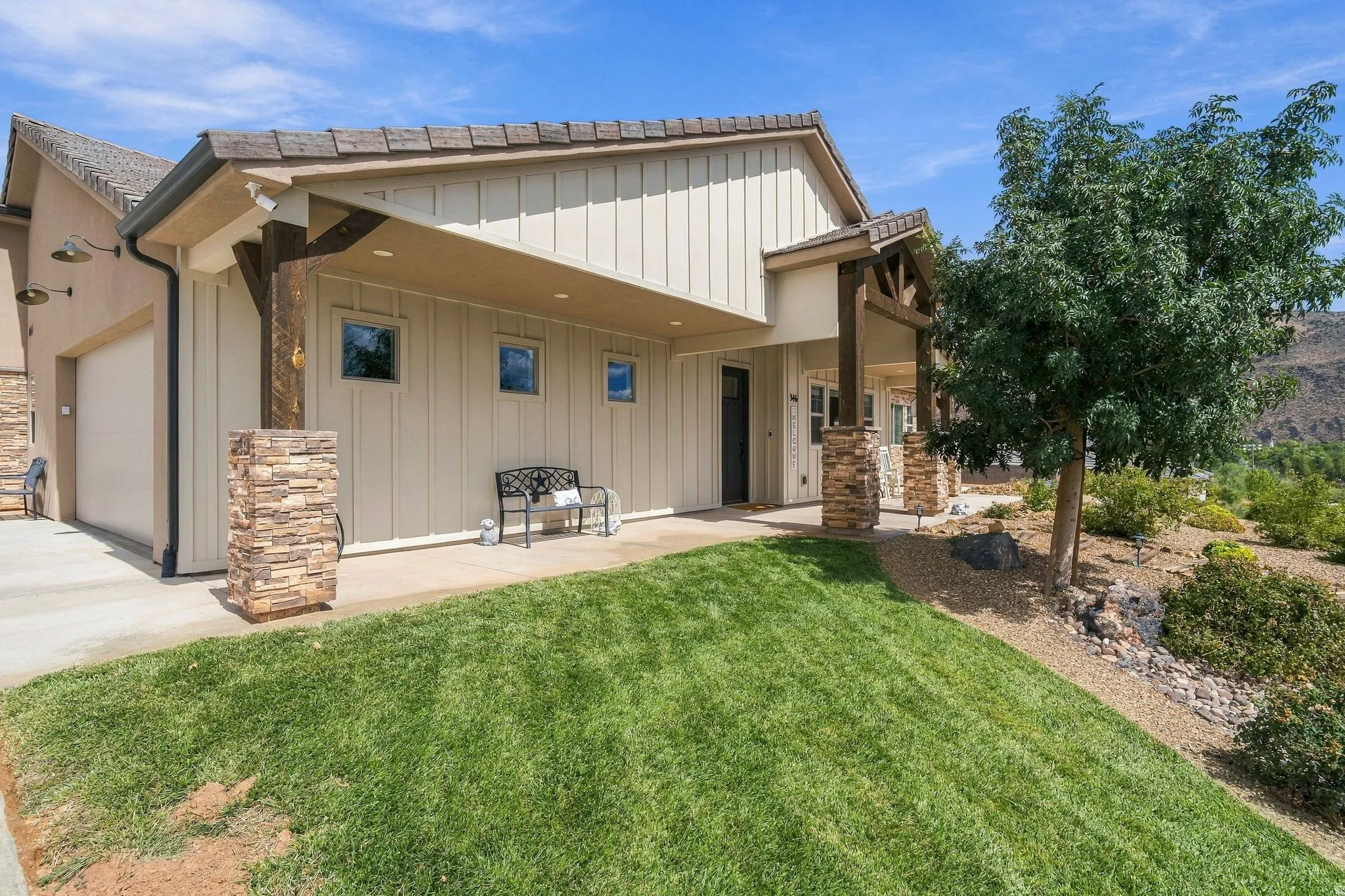 Exterior featuring stone column accents, wood beam detailing, vertical siding, a paved driveway, and an attached garage