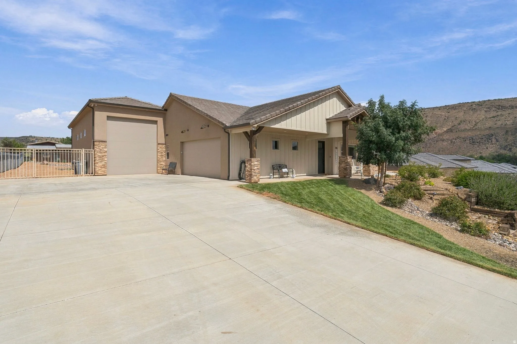 Stucco exterior with stone accents, a covered entry, an attached two-car garage, an additional garage bay, and a sloped lawn with desert landscaping