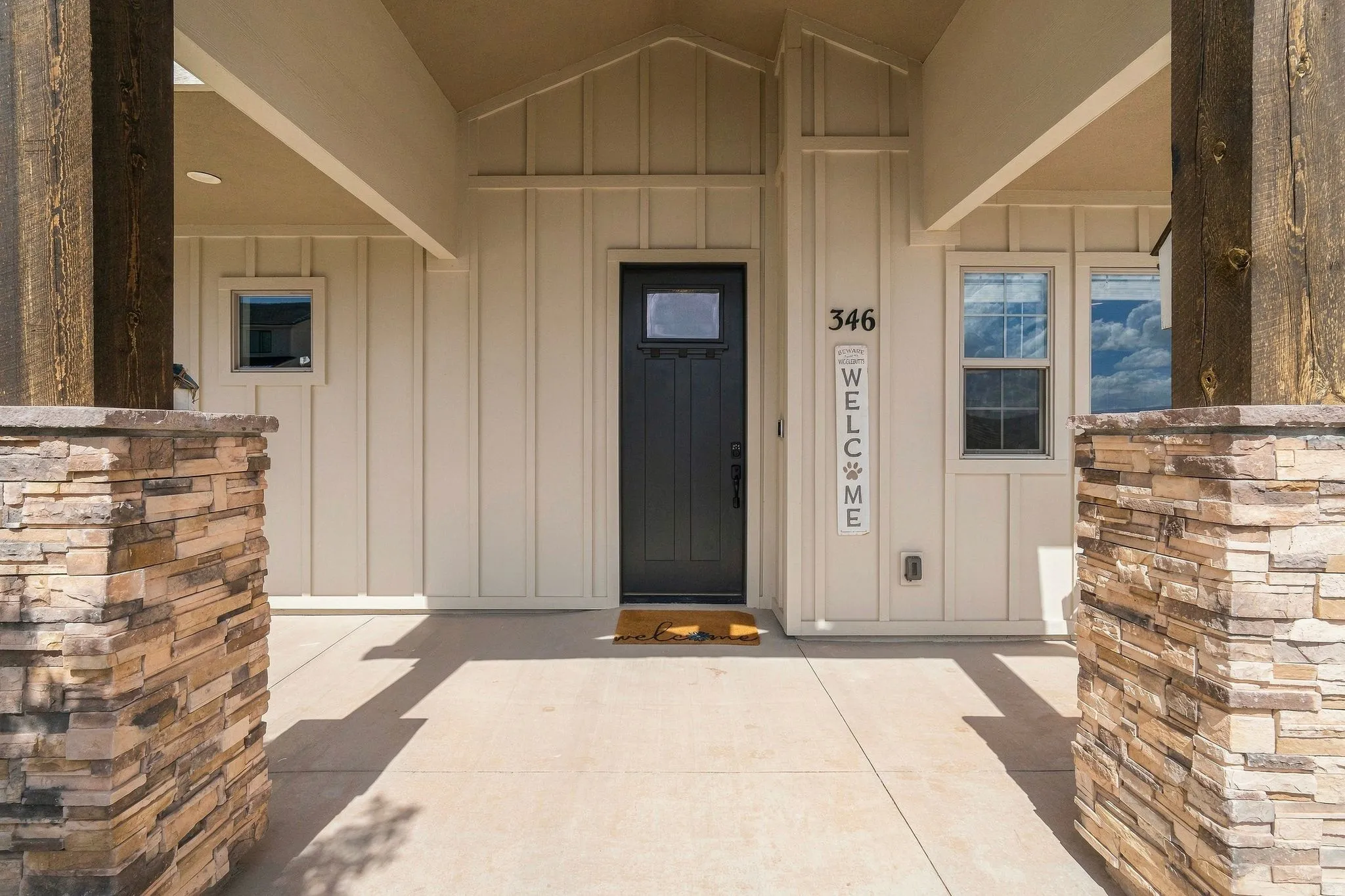 Front entry featuring a dark-paneled door, board and batten siding, stone-clad pillars, and recessed lighting