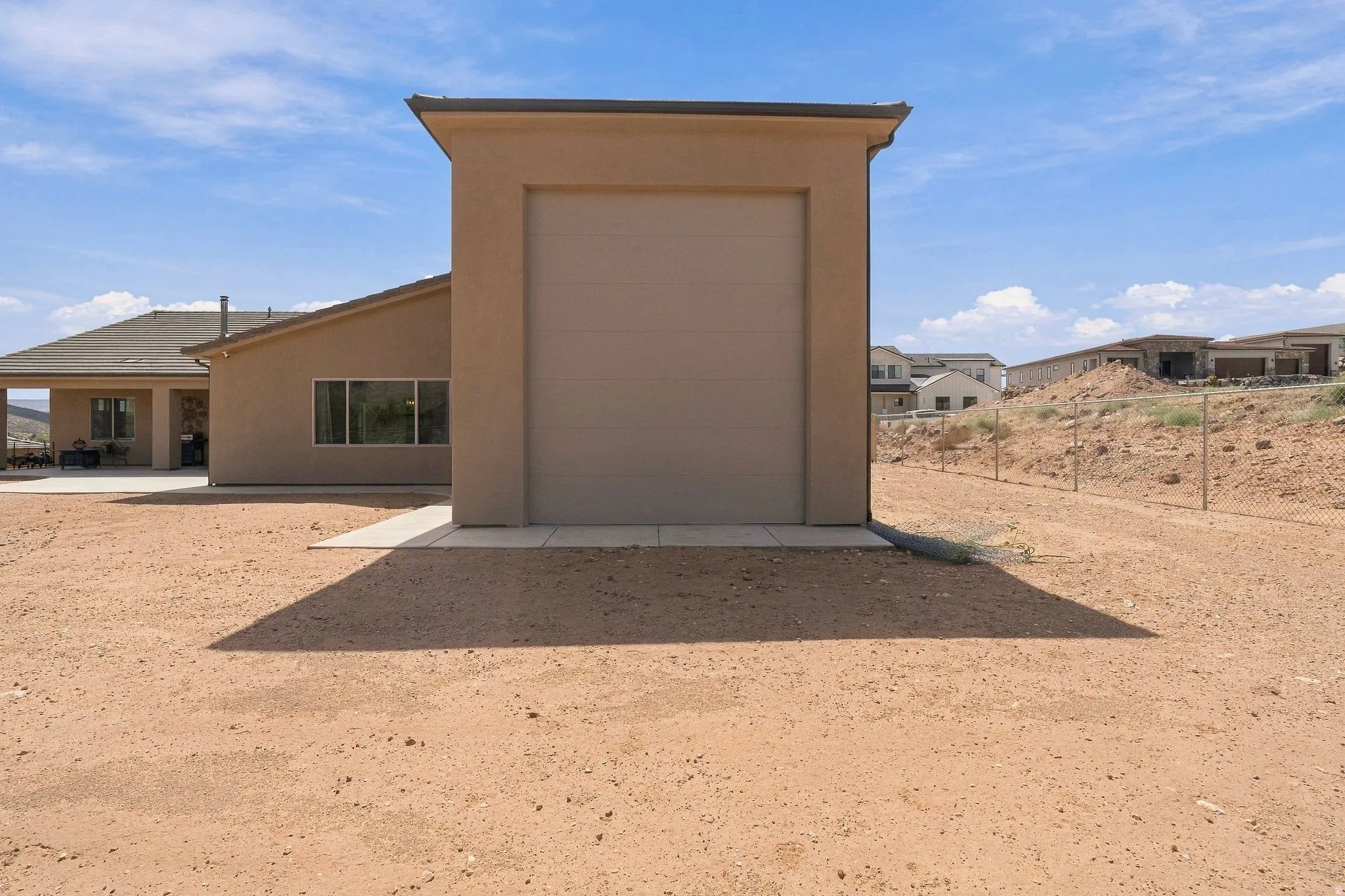 Detached utility building with a roll-up door, adjacent to a stucco-finished residence