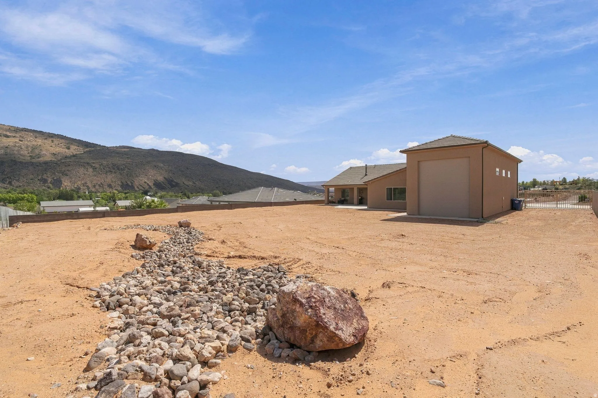 Expansive property featuring a large detached garage with roll-up door, a single-story home with a covered patio, and a stone-lined dry creek bed