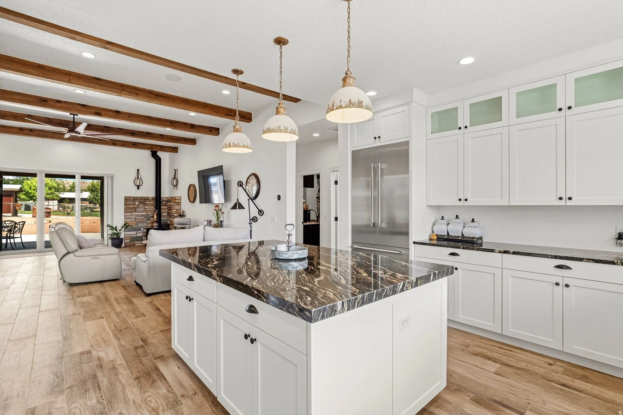 Open-concept living space with exposed wood beams, wood-finish flooring, and a stone-clad fireplace