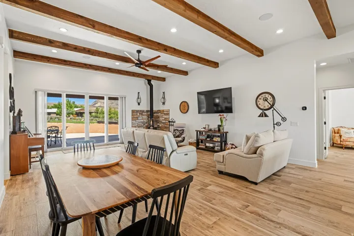 Vaulted ceiling with exposed wood beams, wood-finish flooring, sliding glass patio doors, and a stone-clad fireplace
