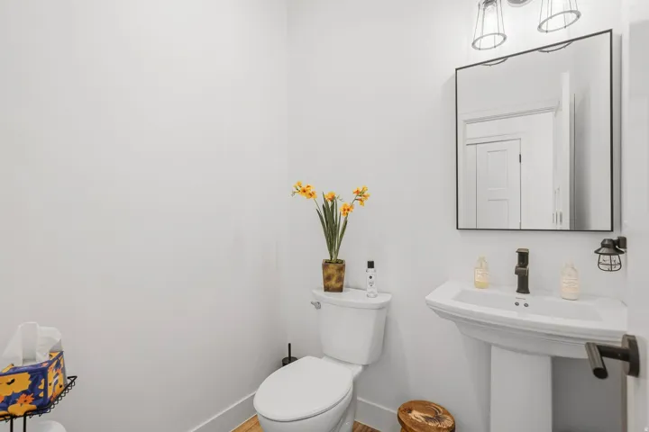 Pedestal sink, wall-mounted mirror, modern wall sconce, oil-rubbed bronze faucet, and wood-finish flooring