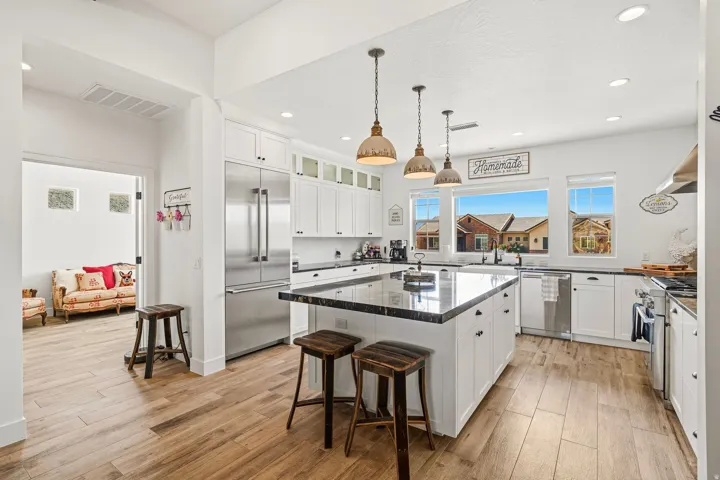 Kitchen featuring white cabinetry, dark countertops, stainless steel appliances, a large central island, and wood-finish flooring